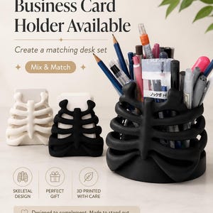 May include: A white business card holder, a black business card holder, and a black cylindrical pencil cup, all featuring a rib cage design. The pencil cup is filled with various pens and pencils. Text includes Business Card Holder Available, Mix & Match, Skeletal Design, Perfect Gift, 3D Printed With Care, and Designed to complement. Made to stand out.