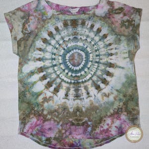May include: A tie-dye t-shirt featuring a circular pattern in green, blue, pink, and brown hues. The short-sleeved top has a scoop neckline. The mandala-style design is centrally placed on the front of the garment.