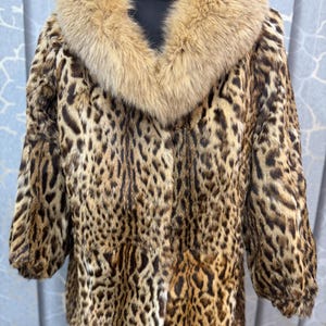 May include: A jacket featuring a brown and black leopard print pattern throughout the body and sleeves, complemented by a large, thick, light brown fur collar that frames the neckline and extends down the front of the garment.