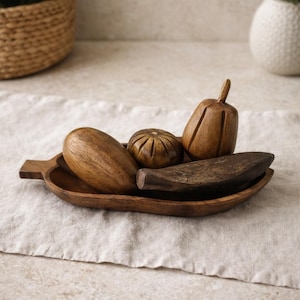 May include: A wooden serving tray holds several carved wooden decorative items. The items include a gourd-shaped piece, a small pumpkin, a pear-shaped item, and a long, curved piece. The tray and items are all a warm brown color.