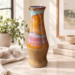 May include: A tall ceramic vase with a flared rim and a tapered neck. The upper portion features a glossy glaze in shades of orange, pink, and turquoise, while the lower base has a textured, speckled brown finish with a matte appearance.