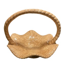 May include: A beige ceramic basket with a woven texture and a curved handle. The basket has a scalloped edge and a detailed pattern on the interior. The handle is also textured, giving it a rope-like appearance.