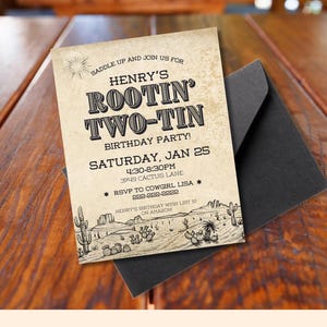 May include: A rustic birthday party invitation with the text "Henry's Rootin' Two-Tin Birthday Party!" on a beige background. The invitation includes the date, time, and RSVP information, along with a desert landscape illustration. It is placed on a black envelope.
