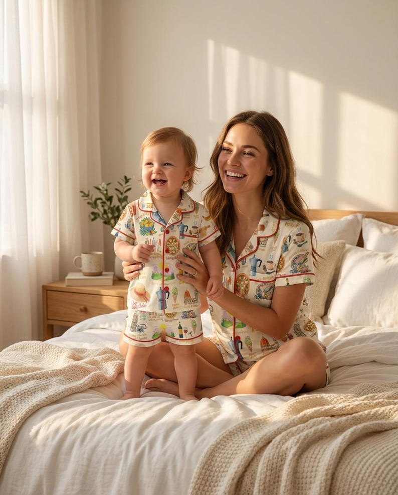 K&ouml;nnte beinhalten: Passende Pyjama-Sets mit cremefarbenem Hintergrund und einem bunten Lebensmittel- und Getr&auml;nkemuster. Die Sets bestehen aus einem kurz&auml;rmeligen Oberteil und Shorts, rot eingefasst. Eine Frau und ein Kind tragen die Pyjamas und l&auml;cheln.