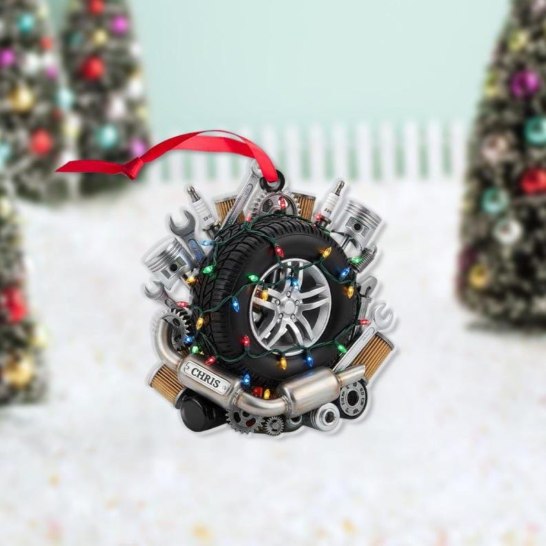 May include: A Christmas ornament shaped like a tire, surrounded by car parts and festive lights. The ornament has a silver rim and a black tire. A red ribbon is attached for hanging. The name "CHRIS" is visible on the ornament.