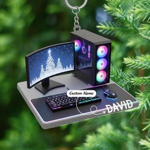 May include: Miniature computer setup ornament with a curved monitor displaying a snowy scene. Includes a keyboard, mouse, and a computer tower with colorful LED lights. The text "Custom Name" and "DAVID" are visible on the mousepad.