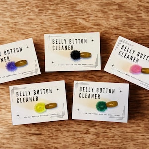 May include: Five cards with the text "Belly Button Cleaner" and a small brush. Each card has a different colored brush: purple, black, pink, yellow, and green. The text "For the person who has everything!" is also on each card.