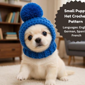 Peut inclure: Un petit chiot blanc portant un chapeau bleu crocheté avec un pompon. Le chapeau couvre la tête et le cou du chiot. Le texte sur une étoile noire indique "Small Puppy Hat Crochet Pattern" et répertorie les langues.
