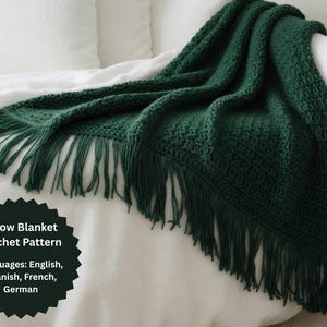 May include: A dark green, crocheted throw blanket with fringe. The blanket is draped over a white surface. The image also includes a dark green graphic with the text "Throw Blanket Crochet Pattern" and lists English, Spanish, French, and German.