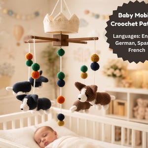 May include: A handmade baby mobile with a crochet crown, wooden arms, and hanging crochet dogs and colorful balls. The mobile is suspended above a baby in a crib. The text on the image says "Baby Mobile Crochet Pattern".