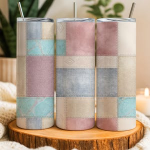 May include: Three stainless steel insulated tumblers with lids and straws. Each tumbler features a patchwork design with squares of pastel colors including pink, blue, beige, and lavender. The tumblers are displayed on a wooden slice.