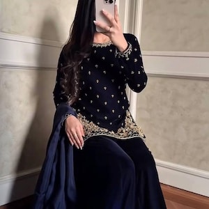 May include: A dark navy blue velvet outfit with gold embroidery. The long-sleeved top and matching pants are embellished with intricate gold designs. A dark blue shawl is draped over the arm. The outfit is suitable for special occasions.