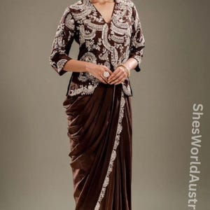 May include: A brown outfit with detailed white embroidery on the top and a draped skirt. The top has a V-neck and three-quarter sleeves. The skirt features a decorative white trim. This outfit is suitable for special occasions.