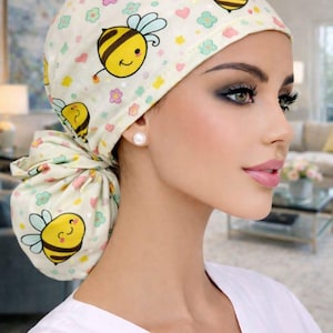 Peut inclure: Un bonnet de chirurgien jaune clair avec un motif répété d'abeilles jaunes souriantes, de fleurs roses, bleues et jaunes. Le bonnet est noué en chignon à l'arrière. Le bonnet est porté par une personne portant un haut blanc.