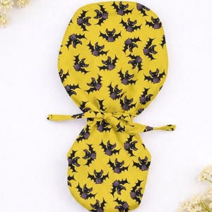 Puede incluir: Una bolsa amarilla con cordón y un patrón repetido de murciélagos negros con detalles morados. La bolsa está atada con una cinta amarilla a juego. Ideal para transportar objetos pequeños.