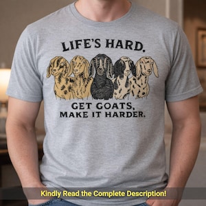 May include: A gray t-shirt featuring the text "LIFE'S HARD. GET GOATS, MAKE IT HARDER." above a row of five goat illustrations. The goats are in various colors, including black, tan, and white. The shirt also has the text "Kindly Read the Complete Description!"