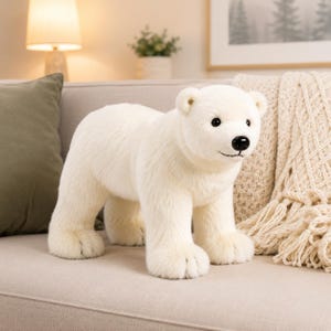 May include: A plush polar bear toy with soft white fur, a black plastic nose, and dark eyes. The stuffed animal is standing in a quadrupedal position, featuring detailed paw pads and a realistic facial expression with a stitched mouth.
