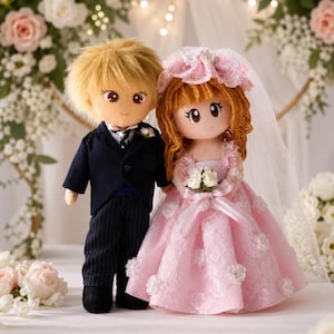 May include: Two plush dolls dressed for a wedding. One doll has short blonde hair, a dark navy blue suit with pinstriped trousers, and a white boutonniere. The other doll has long auburn hair, a pink lace gown with floral accents, and a veil.