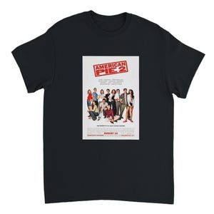 May include: Black t-shirt featuring the movie poster for "American Pie 2." The poster shows a group of people and the movie title in a red and white rectangular box. The movie title is above the group of people. The movie release date is August 10.