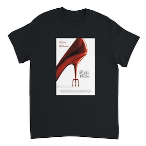 Könnte beinhalten: Schwarzes T-Shirt mit einem Filmposter-Design. Das Poster zeigt einen roten High-Heel-Schuh mit einem Teufelsgabel und den Worten "THE DEVIL WEARS PRADA". Die Namen Meryl Streep und Anne Hathaway sind ebenfalls sichtbar.