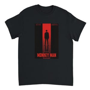 May include: Black t-shirt featuring a movie poster design for "Monkey Man." The poster has a red background with a silhouette of a person standing in a doorway. The movie title is in red text at the bottom.