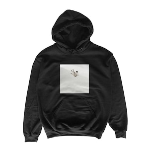 May include: Black hooded sweatshirt with a kangaroo pocket and a drawstring hood. The sweatshirt features a square graphic on the front depicting a person falling. The graphic is in shades of white and gray.