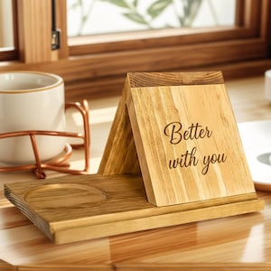 Può includere: Organizzatore da scrivania in legno con finitura naturale. Presenta uno slot per telefono, un'incavo circolare per tazza e una sezione inclinata con la scritta "Better with you".