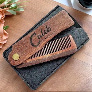 May include: A wooden comb and case set. The comb is made of dark wood and has fine teeth. The case is black and rectangular, with a wooden lid engraved with the name "Caleb" and the word "Groomsman". A small gold-coloured dot is on the lid.