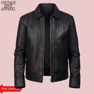 May include: Black leather jacket with a collared neckline and a zipper closure. The jacket has long sleeves and a classic design. The words "VINTAGE HIDE APPAREL" are printed on the top left. The words "FREE SHIPPING" are printed on a red arrow.