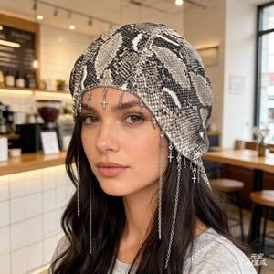 May include: A snake-print beret with dangling silver cross charms. The beret features a pattern of gray, black, and white scales. Silver chains with small crosses hang from the beret's edge, adding a unique touch to this headwear.