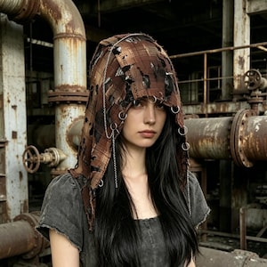 May include: A distressed brown and black plaid hood featuring silver rings and chains. The hood has a torn design. The model is wearing a grey top and has long black hair.