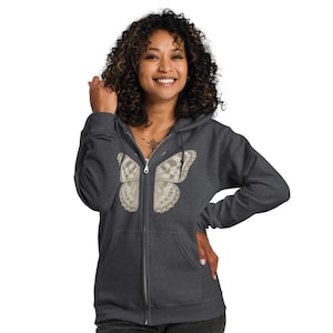 May include: Charcoal gray zip-up hoodie featuring a detailed butterfly wing design on the front. The butterfly wings are in shades of beige and gray. The hoodie has a full zipper and a comfortable fit.