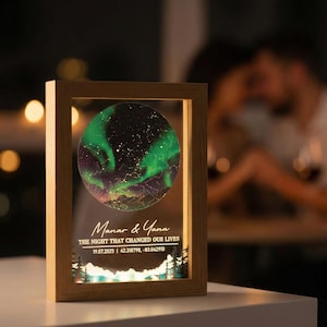May include: A wooden framed night sky art piece with a circular image of the aurora borealis in green and purple. The text "Manar & Yana" and "THE NIGHT THAT CHANGED OUR LIVES" is displayed below the image, along with the date and coordinates.