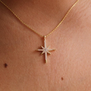 May include: A gold-colored necklace featuring a starburst pendant. The pendant is encrusted with small, sparkling crystals. The necklace is displayed against a skin-toned background, highlighting the jewelry's design and details.