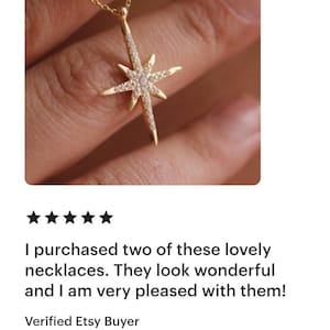 May include: A gold-colored necklace with a starburst pendant, adorned with small, clear gemstones. The necklace is displayed against a neutral background, highlighting the jewelry's design and sparkle.
