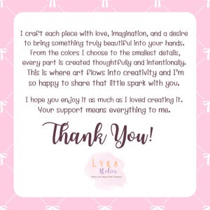 Pu&ograve; includere: Una carta rosa e bianca con la scritta "Thank You!" in corsivo. La carta contiene un messaggio sul processo creativo e il ringraziamento dell'artista per il supporto. Il logo LYKA Atelier si trova in basso.