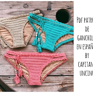 May include: Three crocheted bikini bottoms in beige, turquoise, and pink. The image includes the text "PDF PATRON DE GANCHILLO EN ESPAÑOL BY CAPITANA UNCINO".