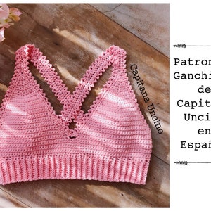 May include: A pink crochet top with a criss-cross strap design. The top has a scalloped edge and is made with a textured stitch. The text "Capitana Uncino" is written in the image.
