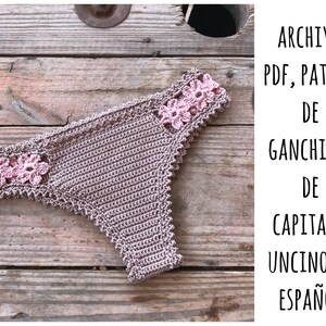 May include: Crochet pattern for a crochet bikini bottom in brown with pink flower accents. The pattern is written in Spanish and is available as a PDF download. The text on the image reads "Archivo PDF, Patron de Ganchillo de Capitana Uncino en Español."