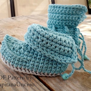 May include: A pair of light blue crocheted baby booties with a white trim and blue beads on the laces. PDF Pattern by CapitanaUncino.