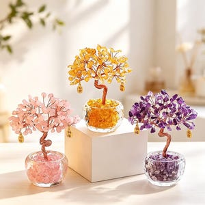 Puede incluir: Tres bonsáis decorativos de alambre con hojas de piedras preciosas en rosa, amarillo y morado. Cada árbol está en un cuenco de cristal transparente lleno de piedras pulidas a juego. Pequeños dijes dorados con caracteres chinos cuelgan de las ramas.