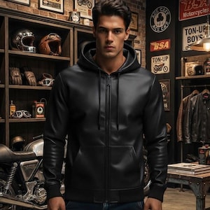 May include: A black leather zip-up hoodie featuring a front zipper closure, a drawstring hood, long sleeves with ribbed cuffs, and a ribbed hem. The garment is paired with dark blue denim jeans, creating a functional and layered look for daily wear.