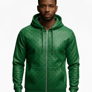 May include: Green zip-up hoodie with a pattern of small, evenly spaced black dots. The hoodie has a drawstring hood, a front pocket, and a silver zipper. The sleeves are long, and the material appears to be leather or a leather-like fabric.