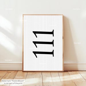 Può includere: Una stampa incorniciata con il numero "111" in un carattere serif nero su sfondo bianco. L'opera è racchiusa in una cornice di legno marrone chiaro, adatta per l'arredamento murale. Lo sfondo presenta un sottile motivo di testo ripetuto.