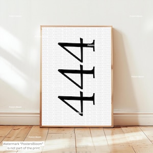 May include: A framed print featuring the number "444" in bold black font. The background is a repeating pattern of inspirational text. The print is displayed on a wooden floor against a white wall.