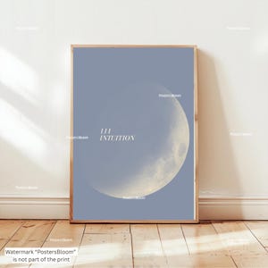 May include: A framed art print featuring a celestial design. The artwork displays a crescent moon against a pale blue background. The text "111 INTUITION" is centered. The frame is a light wood color.