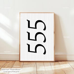 Könnte beinhalten: Gerahmter Kunstdruck mit der Zahl "555" in schwarzer Schrift auf weißem Hintergrund. Der Druck ist in einem hellbraunen Holzrahmen eingefasst und steht auf einem Holzboden.