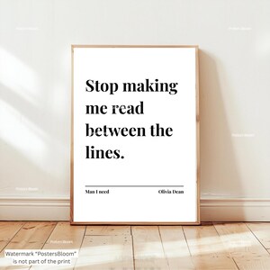 May include: A framed print with the quote "Stop making me read between the lines." in a bold, black font. The print includes the text "Man I need" and "Olivia Dean" in a minimalist design, set against a white background.