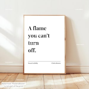 May include: A framed print with the quote "A flame you can't turn off." in black text on a white background. The print also includes the song title "Sweet Lullaby" and the artist "Chris Brown". The frame is a light brown color.