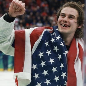 May include: A person smiling and celebrating, draped in an American flag. The flag has red and white stripes and a blue field with white stars. The person is wearing a white jacket.